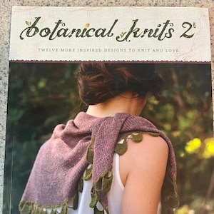 Puede incluir: Una portada de libro con una mujer que lleva una chalina de punto morado y verde con el título "Botanical Knits 2: Twelve More Inspired Designs to Knit and Love" y el autor "By Alana Dakos of Never Not Knitting".