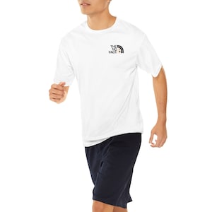 May include: A white short-sleeved t-shirt with a black and white logo that says "THE NORTH FACE" on the front. The person is wearing navy blue shorts.