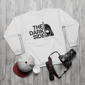 以下が含まれることがあります： 黒いダース・ベイダーのヘルメットと「THE DARK SIDE」の文字が書かれた白いスウェットシャツ。
