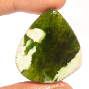 Peut inclure: Une pierre précieuse polie en forme de goutte d'eau, mélangeant des couleurs vert foncé et blanc crème. La pierre présente une surface lisse et brillante avec un motif unique de couleurs tourbillonnantes. De petits points noirs sont dispersés dans les zones vertes.