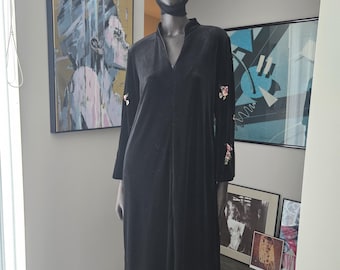 May include: A black velvet maxi dress with floral embroidery on the sleeves. The dress has a V-neckline and a side slit. The mannequin is wearing pink sunglasses and a black headpiece.