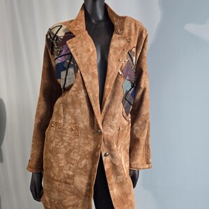May include: A brown suede blazer with a tie-dye pattern, featuring decorative patches on the shoulders and gold-colored stud accents. The blazer has a notched collar, two front pockets, and a single-button closure. The sleeves are long and have buttoned cuffs.