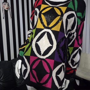 May include: A black sweater featuring a vibrant geometric design in red, yellow, green, purple, and pink. The pattern incorporates white circles and diamond shapes, with black sequins. The sweater is displayed on a mannequin.