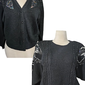 May include: Two black sweaters with beaded embellishments. The sweater on the top has a v-neck and buttons down the front. The sweater on the bottom has a round neck and a cable knit pattern.