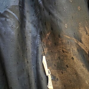 May include: Close-up of the inside lining of a dark navy blue garment. The fabric has a subtle sheen and is patterned with small, evenly spaced diamond shapes. A white tag with text is attached to the seam.