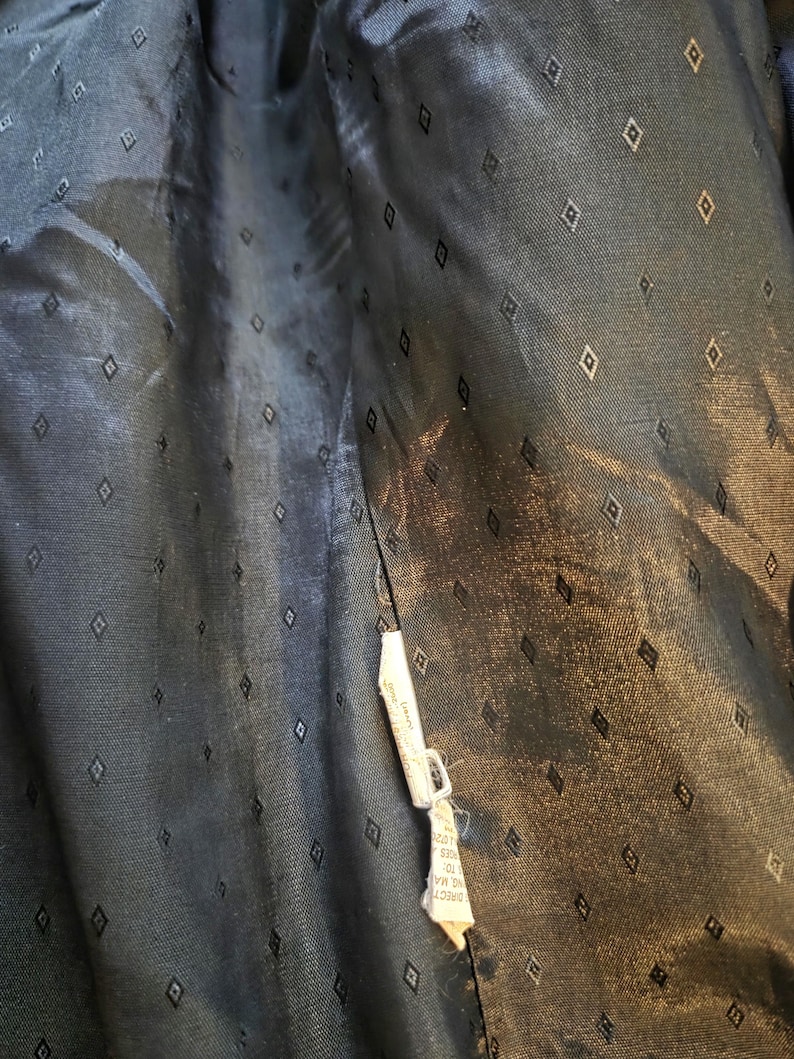 May include: Close-up of the inside lining of a dark navy blue garment. The fabric has a subtle sheen and is patterned with small, evenly spaced diamond shapes. A white tag with text is attached to the seam.