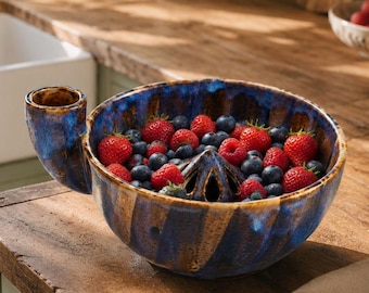 May include: A ceramic citrus juicer bowl with a deep blue and tan glazed finish, featuring a central reamer and a side handle. The bowl is filled with a mixture of fresh red strawberries and small blue blueberries, showcasing a ribbed exterior texture.