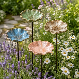 May include: Four ceramic flower-shaped garden stakes in light green, blue, beige, and pink. Each dish-like top features a ruffled edge and a speckled, textured finish, mounted on a thin, dark metal rod for placement in a garden bed.