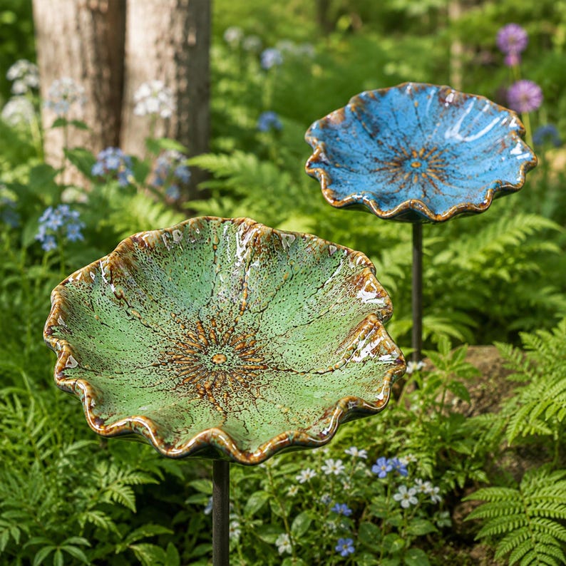 K&ouml;nnte beinhalten: Zwei Gartenstecker aus Keramik mit breiten, gewellten, bl&uuml;tenf&ouml;rmigen Schalen. Eine Schale ist hellgr&uuml;n gesprenkelt mit braunen R&auml;ndern, die andere blau gesprenkelt mit braunen R&auml;ndern. Jede Schale ist auf einem d&uuml;nnen, dunklen Metallstab montiert.