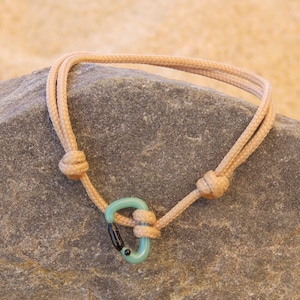 May include: A light brown rope bracelet with a green and black carabiner clasp.