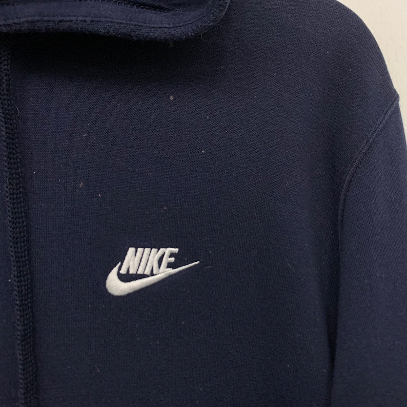 May include: Navy blue hooded sweatshirt with a white embroidered Nike logo. The sweatshirt features a drawstring and a high collar. The material appears to be soft and comfortable.