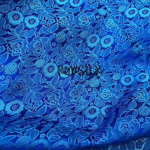 May include: Blue fabric with a floral pattern. The fabric has a raised texture and a repeating pattern of small flowers and leaves.