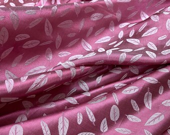May include: Pink satin fabric with a white leaf pattern. The fabric is soft and has a subtle sheen.