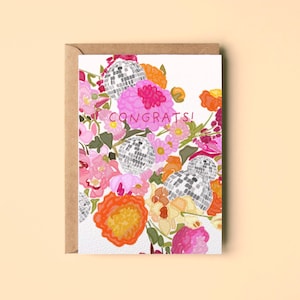 Könnte beinhalten: Eine Grußkarte mit einer farbenfrohen Illustration aus rosa und orangefarbenen Blumen, durchsetzt mit silbernen Discokugeln. Der Text CONGRATS! ist in Pink in der Mitte aufgedruckt. Die Karte steckt in einem braunen Kraftpapierumschlag.