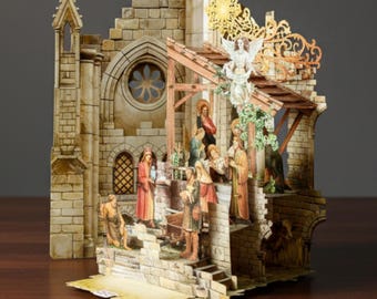 May include: A detailed, three-dimensional nativity scene depicting the birth of Jesus. The scene is set within a stone structure with figures of Mary, Joseph, and the baby Jesus, along with angels and other biblical characters. The color palette includes beige, brown, and touches of gold.