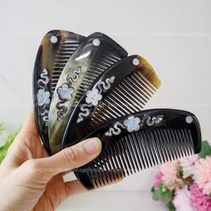 Puede incluir: Se muestran cuatro peines decorativos en tonos marrón y negro. Cada peine presenta un diseño único con patrones florales y ondulados blancos. Los peines se sostienen en una mano, destacando su elegancia y artesanía.