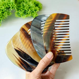 Puede incluir: Una colección de peines de cuerno en varios tonos de marrón, beige y gris. Los peines tienen una forma curva con dientes espaciados uniformemente. La imagen está bien iluminada, mostrando los patrones y texturas naturales del material de cuerno.