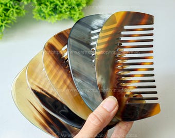 May include: A collection of horn combs in various shades of brown, tan, and gray. The combs have a curved shape with evenly spaced teeth. The image is well-lit, showcasing the natural patterns and textures of the horn material.