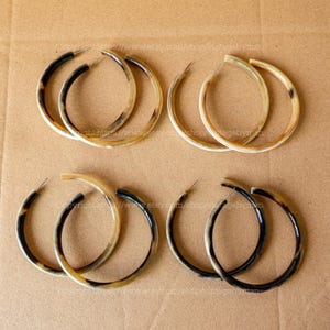May include: Four pairs of large hoop earrings made of brown and black horn. The earrings are all the same size and shape, and they are arranged in two rows of two.