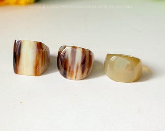 Könnte beinhalten: Drei Ringe aus braunem und weißem Horn. Die Ringe sind alle unterschiedlich groß und haben eine glatte, polierte Oberfläche.