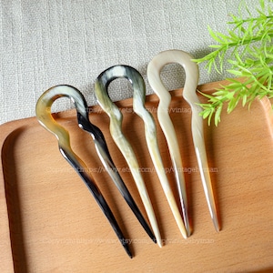Può includere: Quattro pettini per capelli marroni e neri con un anello in cima. I pettini sono fatti di corno e sono disposti su una superficie di legno.