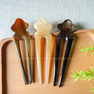 May include: Three decorative hair combs made of brown, black, and light brown horn. The combs have a unique design with a decorative top and two prongs.