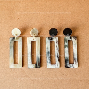 May include: Four pairs of rectangular horn earrings with a black, white, and brown mottled pattern. The earrings are made of natural horn and have a simple, elegant design.