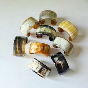 May include: A collection of ten horn bracelets in various shades of brown, black, and white. The bracelets are all made from natural horn and have a unique, organic look.
