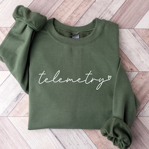 May include: A green sweatshirt with the text "telemetry" in white cursive lettering and a small white heart.