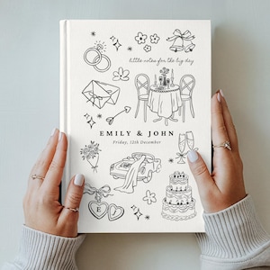 May include: A white hardcover book with black line art illustrations of wedding icons including rings, a table setting, a car, and a cake. The text reads little notes for the big day, EMILY & JOHN, and Friday, 12th December, in a clean font.
