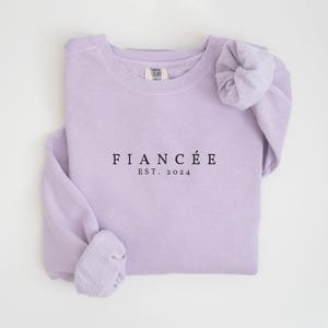 May include: A lavender sweatshirt with the text "FIANC&Eacute;&Eacute; EST. 2024" printed on the front.