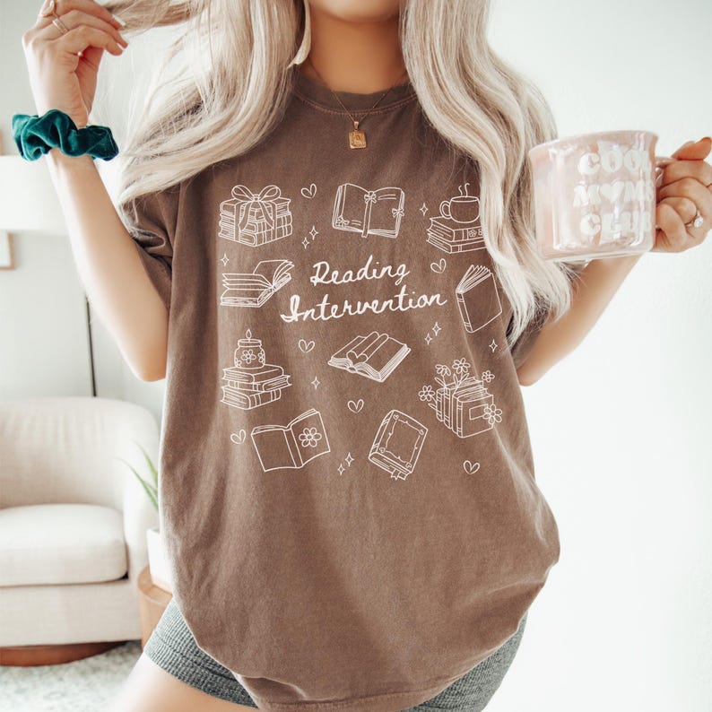 May include: A brown t-shirt with a white graphic design of books and the text "Reading Intervention".