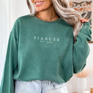 May include: A green sweatshirt with the text "Fianc&eacute;e Est. 2024" in white.