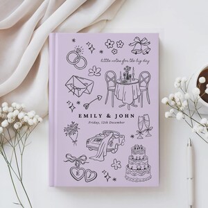 May include: A light purple hardcover journal featuring black line art illustrations of wedding-themed icons including rings, a table setting, a car, a cake, and flowers. The text reads "little notes for the big day", "EMILY & JOHN", and "Friday, 12th December".