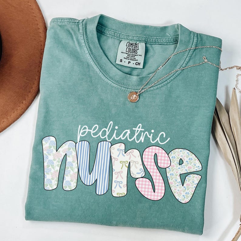 Op de afbeelding: Een tealblauw t-shirt met de woorden "pediatric nurse" in witte letters. Het woord "nurse" is gemaakt van kleurrijke patchwork-vierkanten met bloemen- en ruitpatronen.