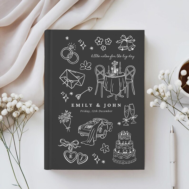 May include: A dark gray hardcover notebook featuring white line art illustrations of wedding icons including rings, a table setting, a car, and a cake. The text reads "little notes for the big day", "EMILY & JOHN", and "Friday, 12th December".