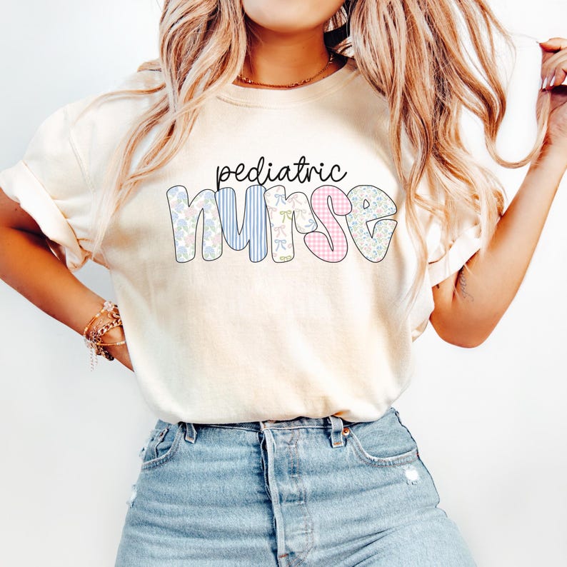 Op de afbeelding: Een wit T-shirt met de tekst "pediatric nurse" in kleurrijke, gepatroneerde letters. De letters zijn in patchwork-stijl met verschillende bloemen- en geometrische patronen.