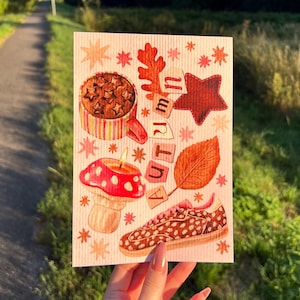Könnte beinhalten: Eine rechteckige Grußkarte mit einer vertikalen Anordnung herbstlicher Illustrationen, darunter ein gestreifter Becher mit Sternenmuster, ein roter Pilz, ein brauner Sneaker, ein Eichenblatt und das in Blockbuchstaben geschriebene Wort AUTUMN.