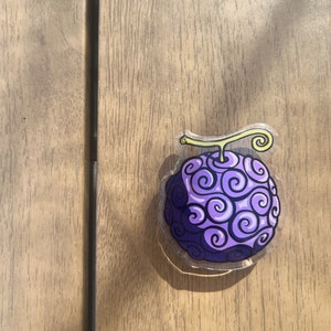 Puede incluir: Una fruta de dibujos animados de color morado y amarillo con un patrón de espiral. La fruta está sobre un fondo de madera.