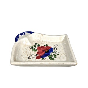 May include: A white ceramic dish with a blue rim and a floral design. The dish has a crackled glaze and features a red and blue flower with green leaves.