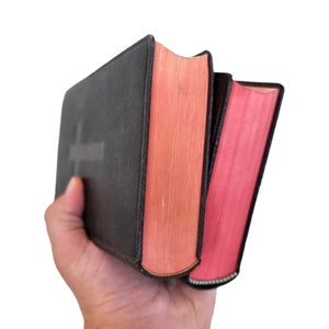 May include: Two black leather-bound books with red and pink pages. The top book has a cross embossed on the cover.
