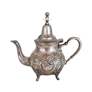 Puede incluir: Una tetera de plata con un diseño ornamentado y un pequeño pomo en la tapa. La tetera tiene un cuerpo redondeado y un pico curvo.