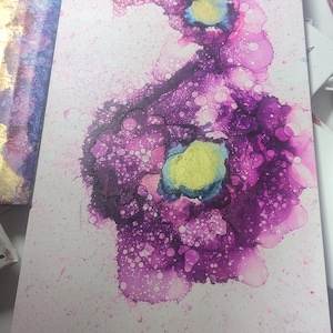 Op de afbeelding: Abstract schilderij op canvas in roze, paarse en gouden kleuren. Het schilderij heeft een draaiend ontwerp met een grote, centrale cirkel.
