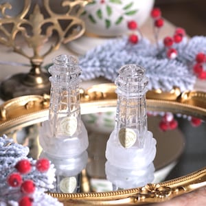 Può includere: Due saliere e pepiere in vetro trasparente a forma di faro su un vassoio dorato con una base bianca opaca. Le saliere sono decorate con il logo Lenox.