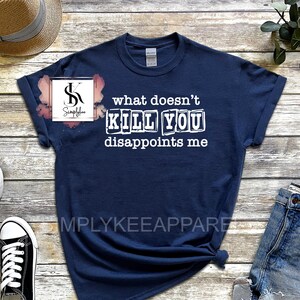 May include: A navy blue t-shirt with white text that reads "what doesn't kill you disappoints me". The text is in a blocky font and appears to be printed on a distressed fabric.
