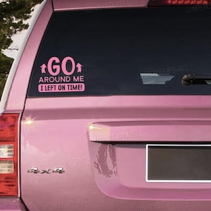 May include: A pink car with a pink sticker on the rear window. The sticker reads "GO AROUND ME I LEFT ON TIME!" in pink text with arrows. The car has a 4x4 emblem.