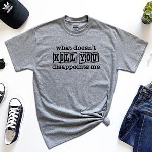 May include: A gray t-shirt with the text "what doesn't kill you disappoints me" printed in black. The text is in a blocky font and appears to be stamped on the shirt.