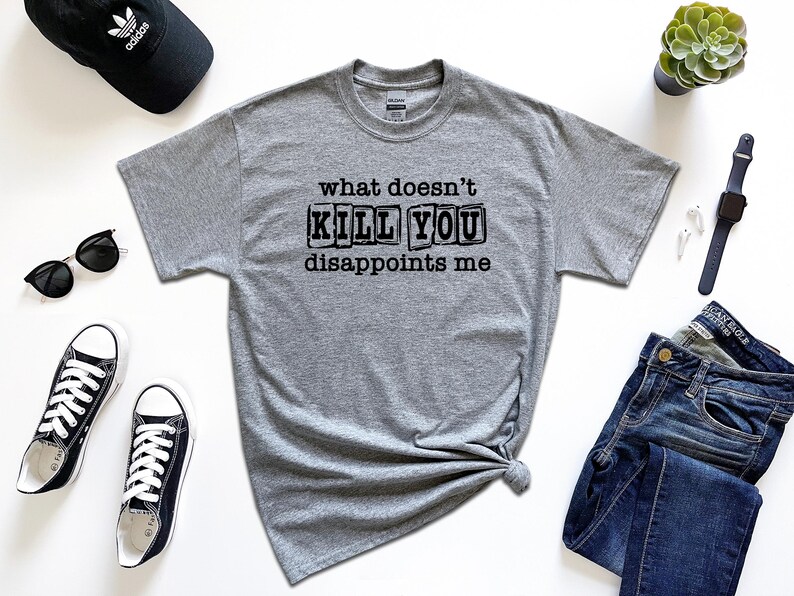 May include: A gray t-shirt with the text "what doesn't kill you disappoints me" printed in black. The text is in a blocky font and appears to be stamped on the shirt.