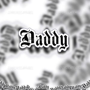 May include: A black and white sticker with the word "Daddy" in a gothic font. The sticker has a white border and is surrounded by blurred images of the same sticker. The text "SIMPLYKEE APPAREL" is also visible.