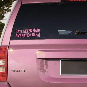 May include: Pink car window decal with the text "HATE NEVER MADE ANY NATION GREAT" in a bold, sans-serif font. The decal is applied to the rear window of a pink SUV. The words "SIMPLYKEE APPAREL" are also visible.